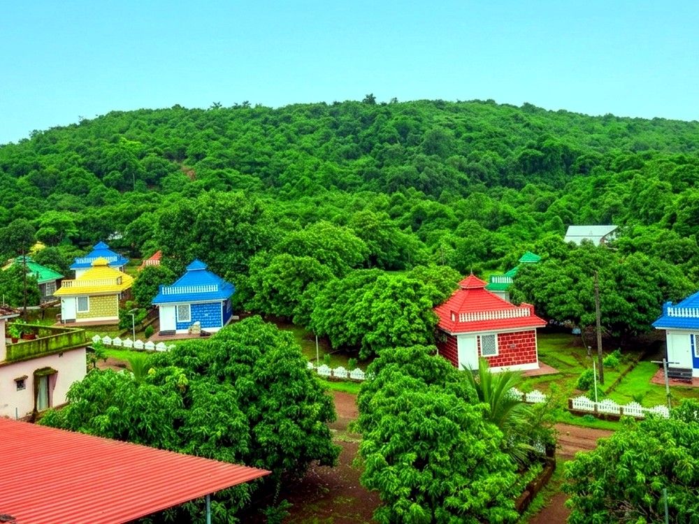 Aerial view of Aranya Kutir's cottages amid mango orchard and forest hill